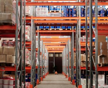 Interior de almacén de fulfillment FBA con estanterías de inventario y cajas de pedidos apiladas en pasillos