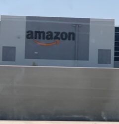 Logo de Amazon en el exterior de un centro de fulfillment con camiones de reparto y cielo despejado