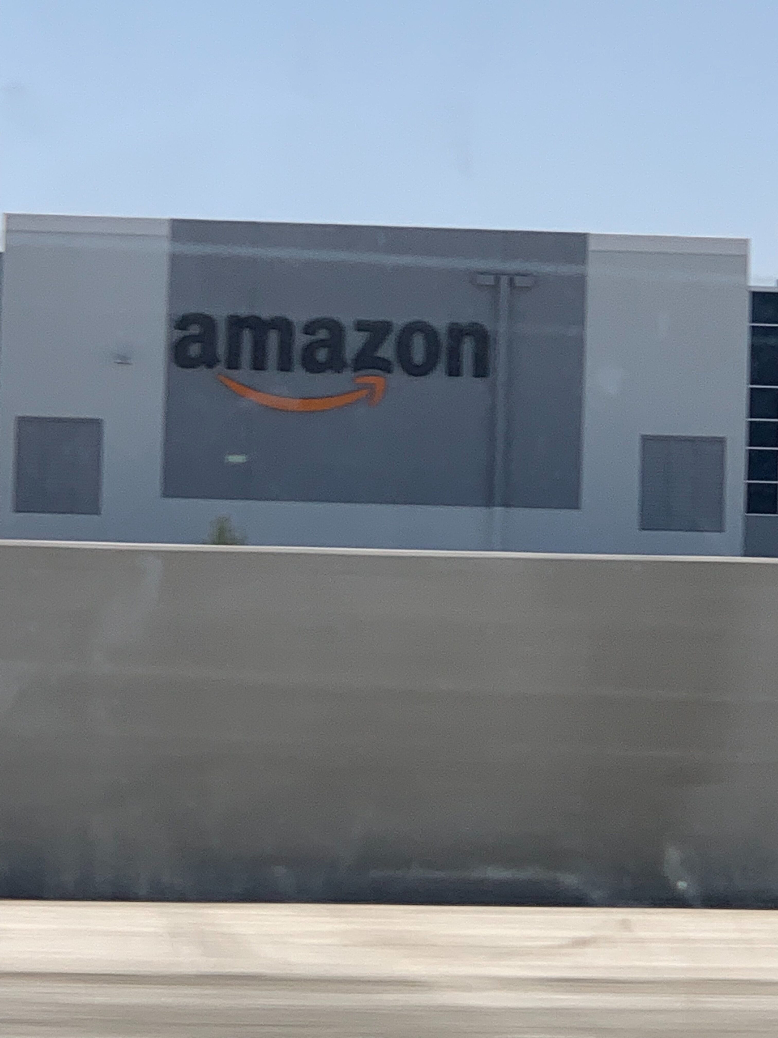 Logo de Amazon en el exterior de un centro de fulfillment con camiones de reparto y cielo despejado